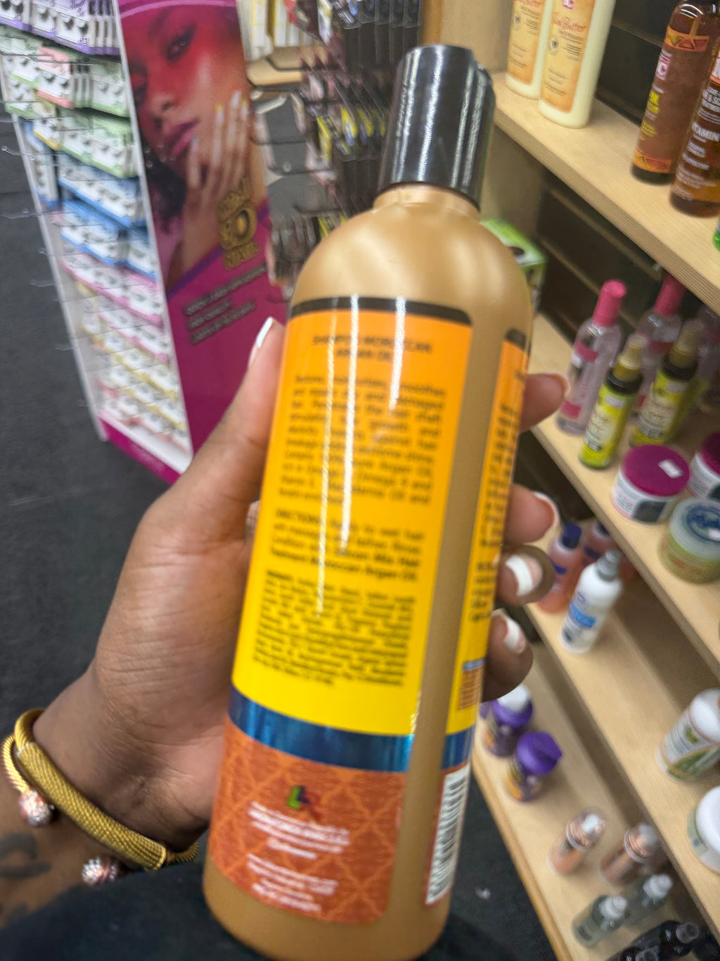 A hand holding a large bottle of hair product in a retail store setting, with shelves of other items in the background.