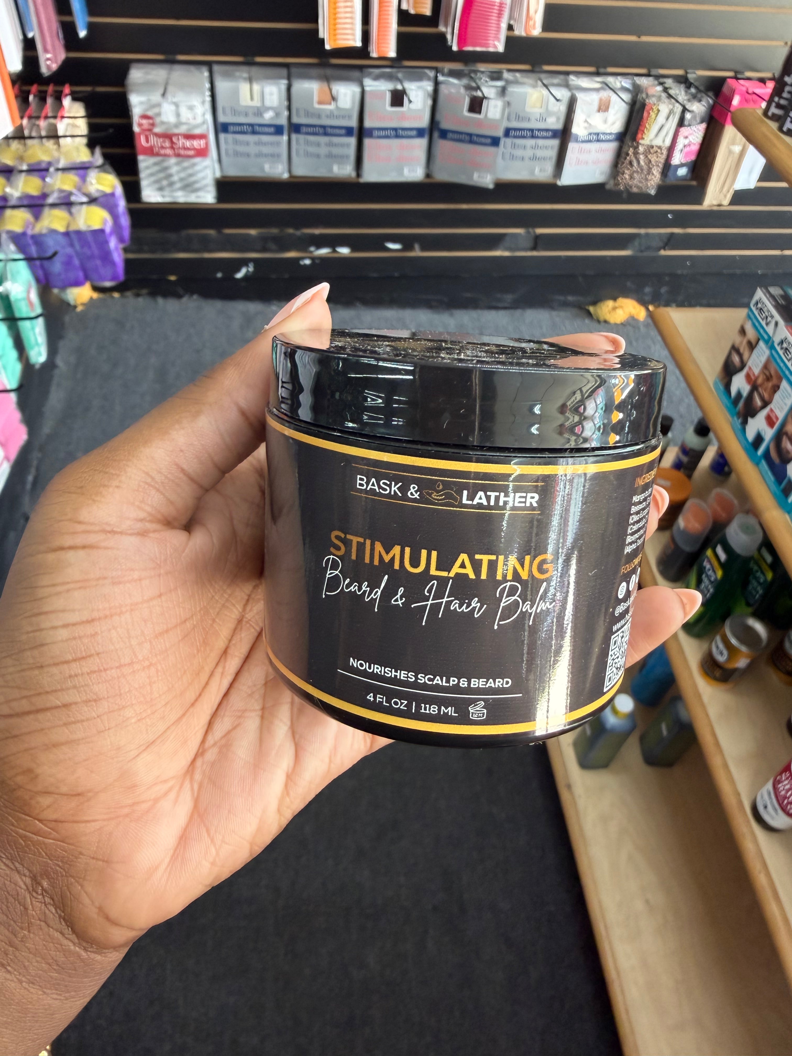 A hand holding a jar of Bask & Leather Stimulating Beard & Hair Balm in a retail store setting.
