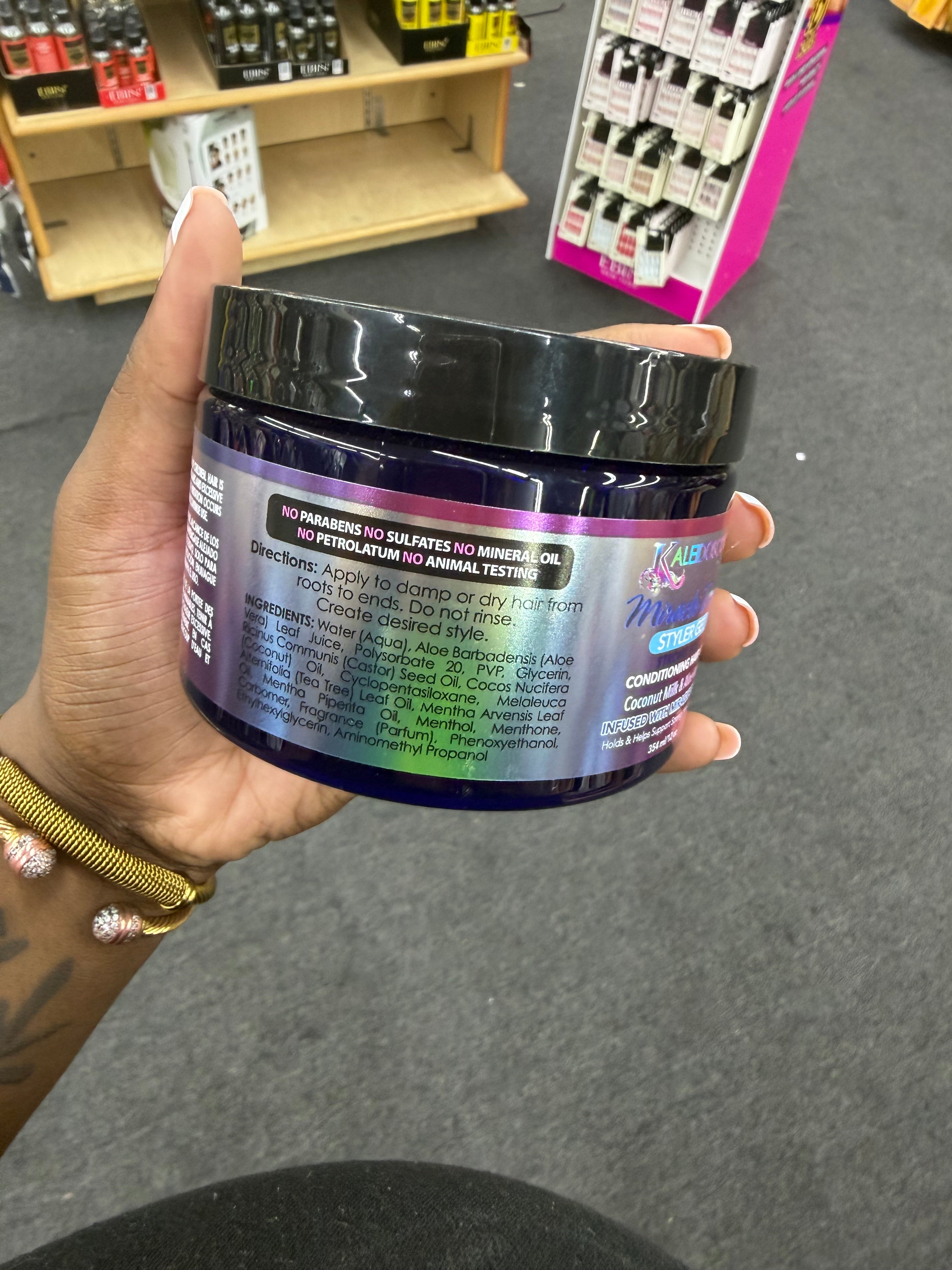 A hand holding a dark purple jar of hair product with a black lid, photographed in a retail store setting with shelves and display signs in the background.