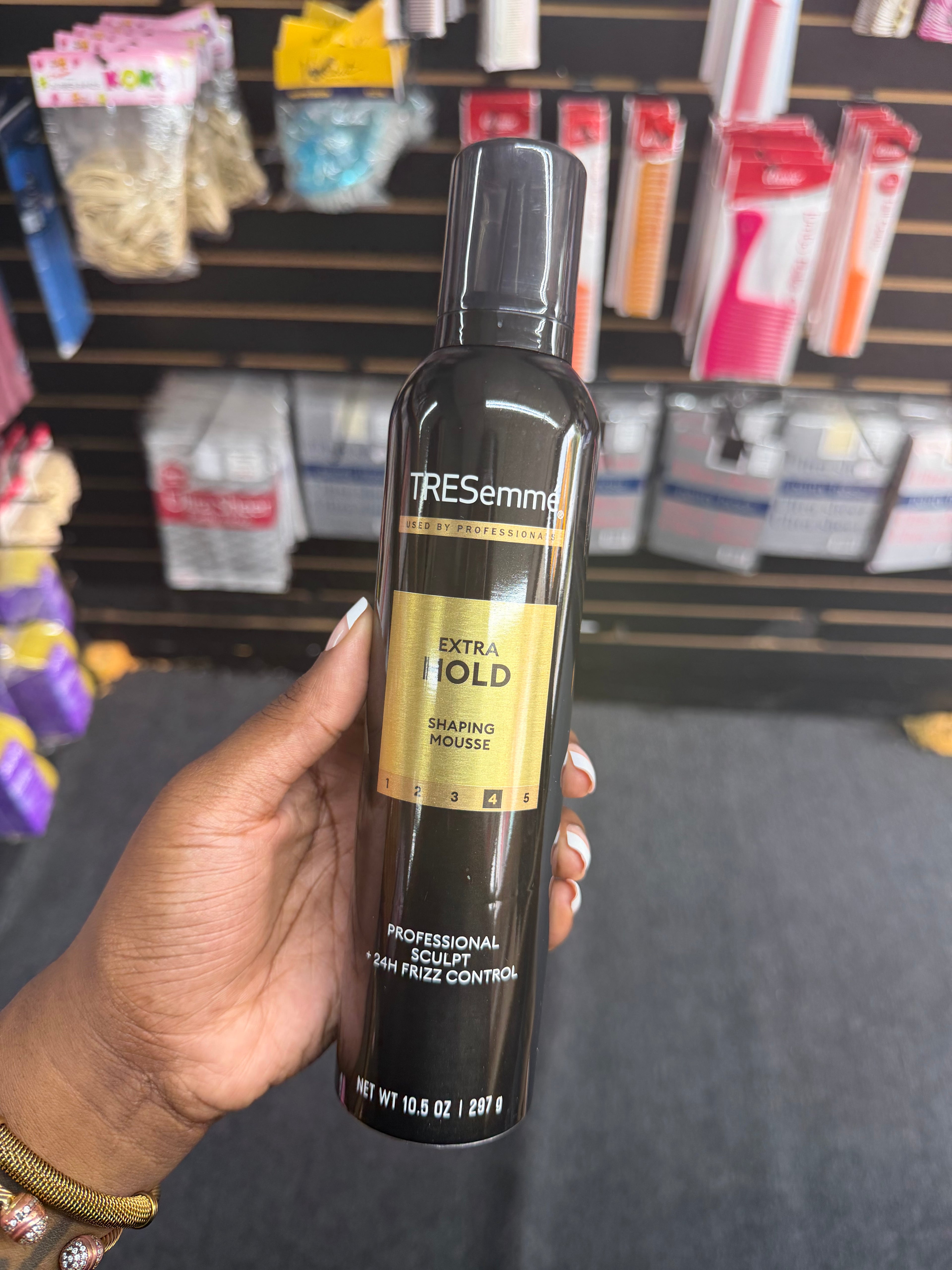 A hand holding a bottle of TRESemmé Extra Hold Shaping Powder in a retail store setting.