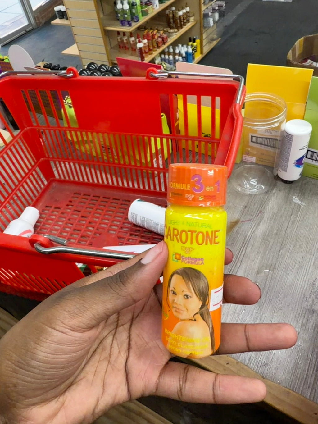 A hand holding a small bottle of Arotone hair growth serum in front of a red shopping basket on a store counter.