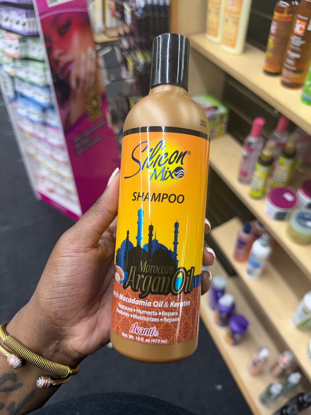 A hand holding a bottle of Salon Mix Morocco Argan Oil Shampoo in a retail store setting with shelves of other products in the background.