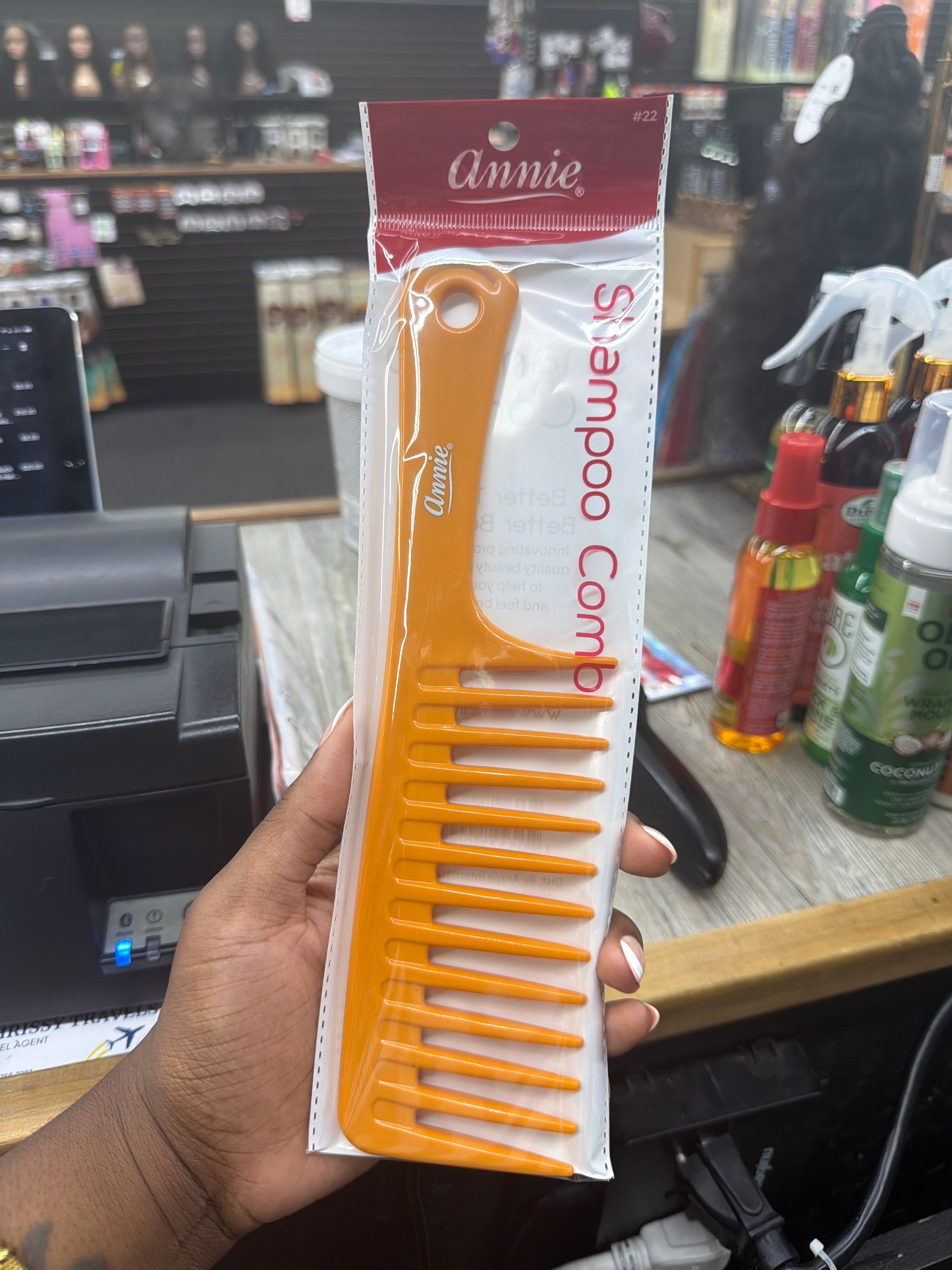 Annie brand orange wide-tooth shampoo comb in its original retail packaging, held by a hand in a retail store setting.