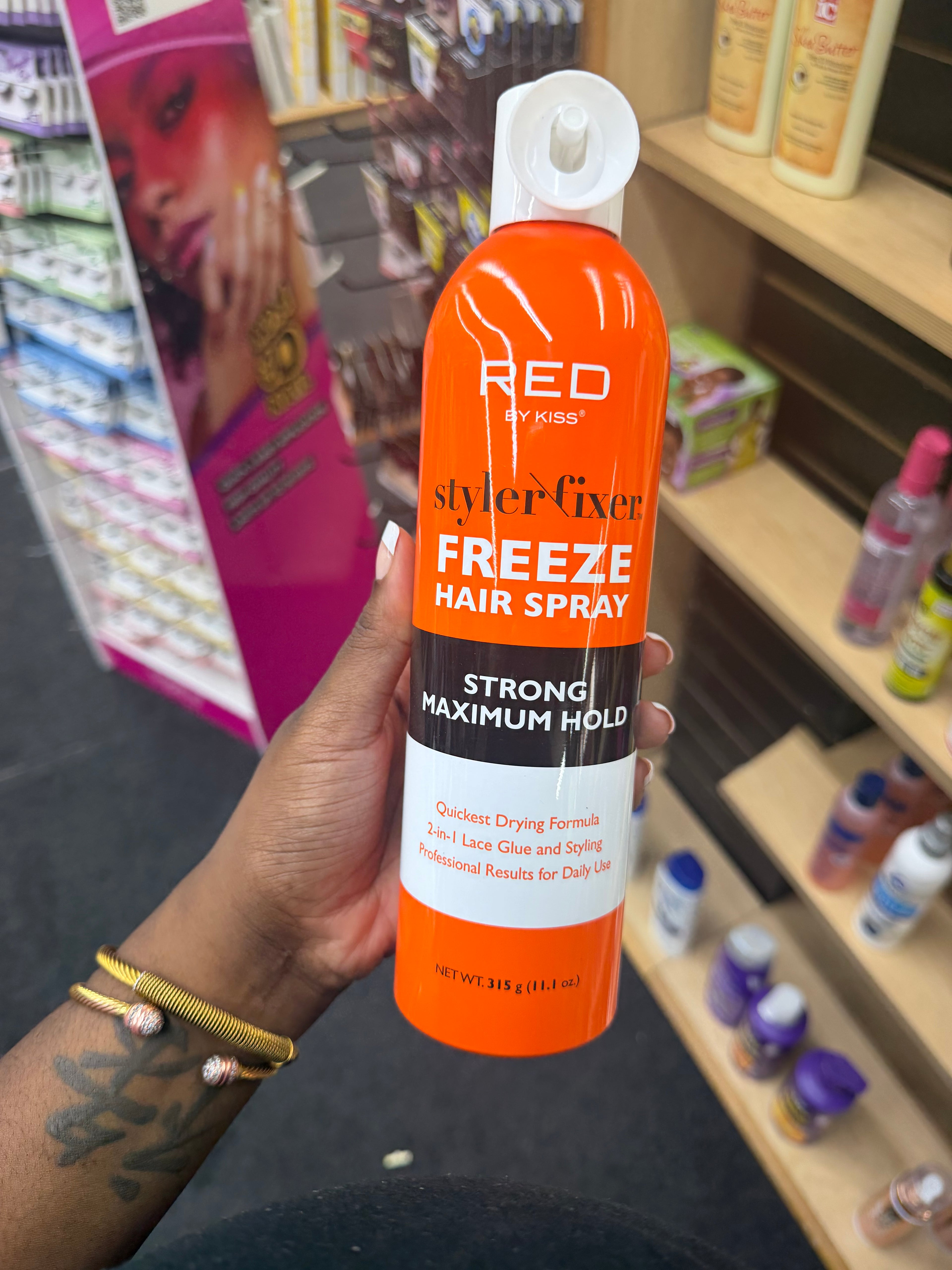 A hand holding a bottle of Red Eyebrow Styler Fixer Freeze Hair Spray in a retail store setting.