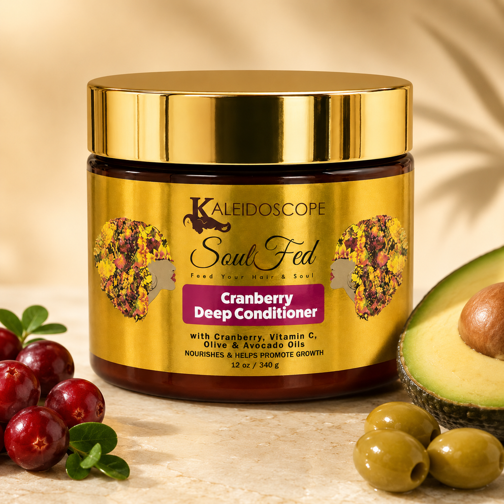 A jar of Kaleidoscope Soul Fed Cranberry Deep Conditioner with a shiny gold lid and gold label, styled on a beige surface with cranberries, olives, and an avocado half in the foreground.