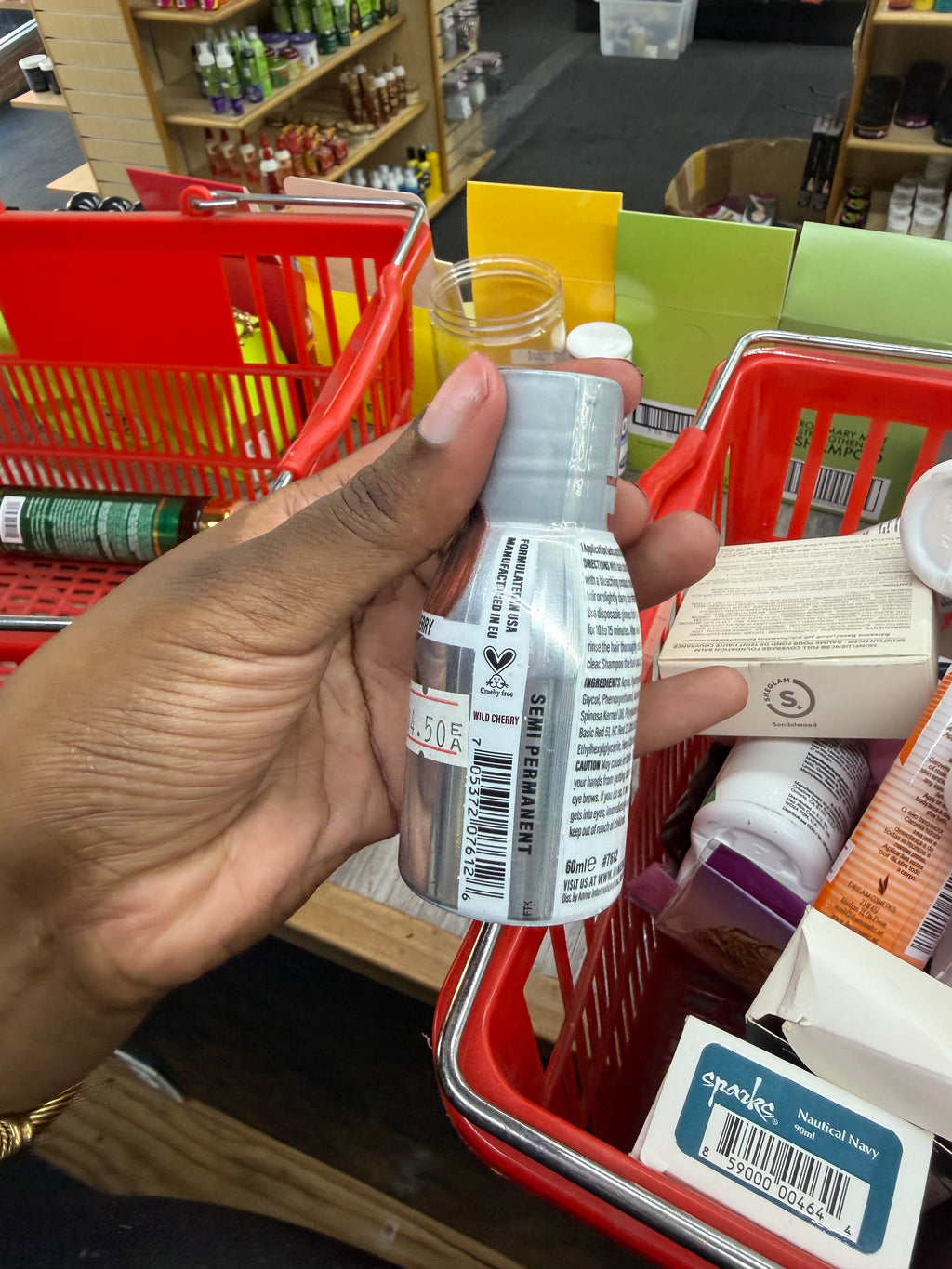 A hand holding a small clear bottle with a white cap and a white product label inside a red shopping basket in a retail store.
