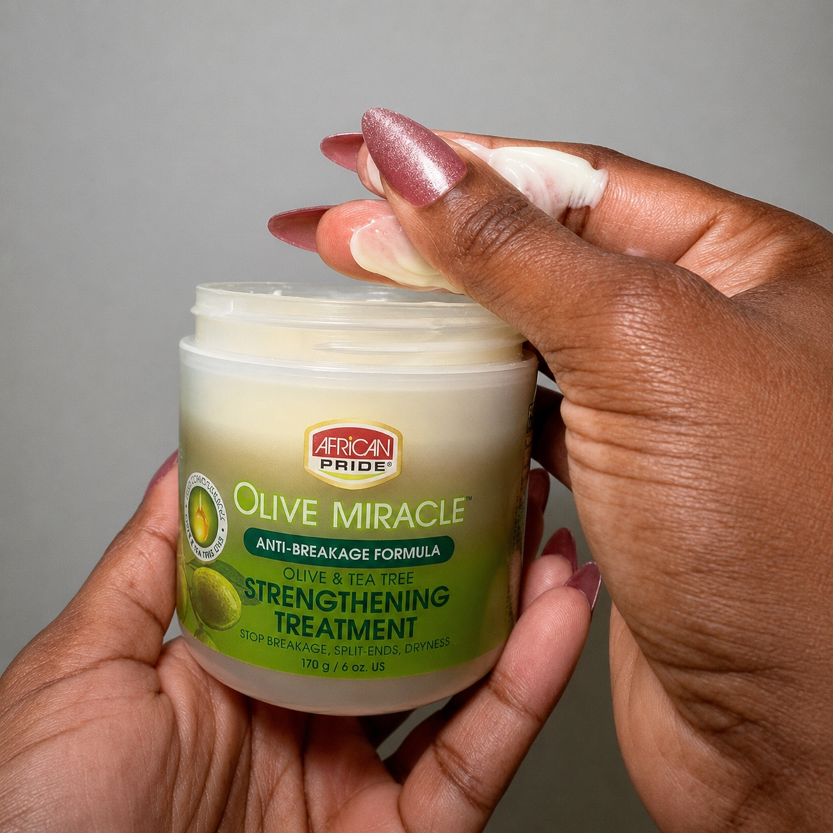 African Pride Olive Miracle Strengthening Treatment open jar showing creamy hair treatment texture being applied by hand